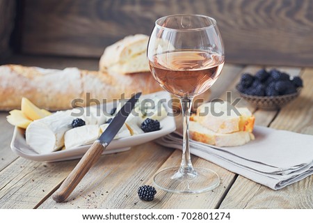 A glass of rose wine served with cheese plate, blackberries and baguette. Assortment of cheese with berries on wooden background. Royalty-Free Stock Photo #702801274