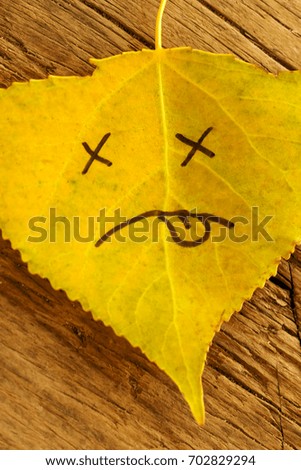 Yellow leaf with a picture of a sad face on the old wooden background with cracks