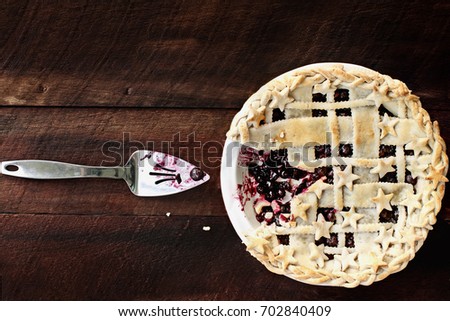 Top view of a blueberry pie with lattice and stars crust over a rustic wooden background. A slice of the pie is missing. Image shot from above.