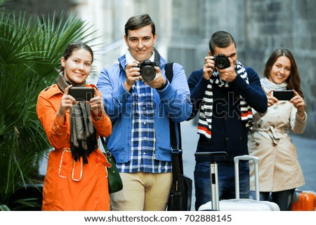 Group of positive young friends walking through street with camera and smartphone. Focus on the left couple