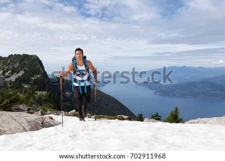 Latin American Male Adventurer is hiking on top of snow during a sunny summer day. Picture taken on the way up to The Lions Mountain in Lions Bay, North of Vancouver, British Columbia, Canada.