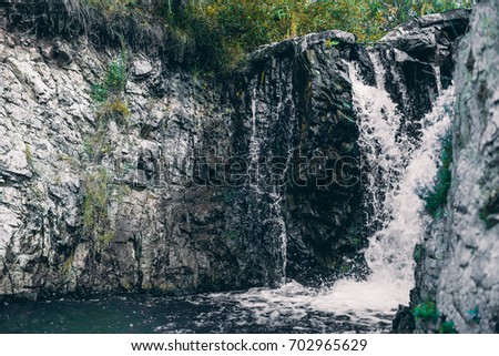 View of beautiful low waterfall in mossy cliffs: two streams of water go into one during falling down into foam and becoming small river, Russia, Altai mountains