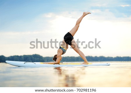 Side view picture of a young woman on paddle board practicing three legged down Dog yoga pose