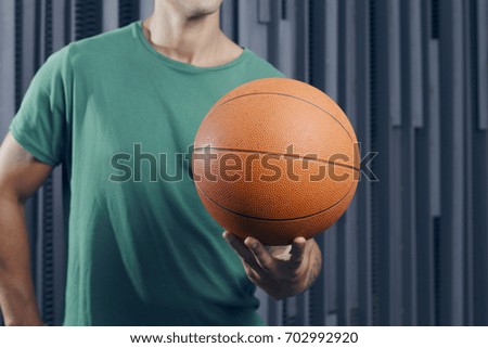 Confident man standing over a metallic background, with a basket ball, outdoors.