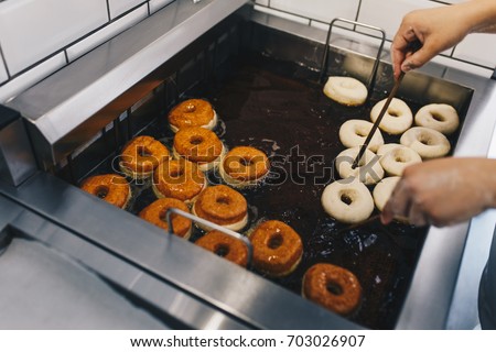 Procedure of making donuts in a small town donut bakery - putting donuts in a deep fryer. Selective focus. Royalty-Free Stock Photo #703026907