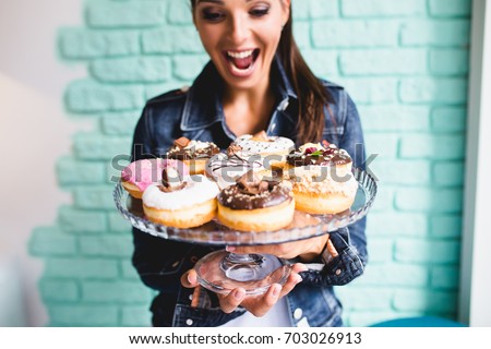 Beautiful young woman enjoying in delicious glazed and decorated donuts. Selective focus. Royalty-Free Stock Photo #703026913