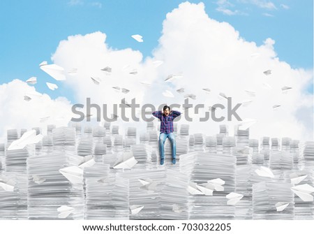 Young man in casual clothing sitting on pile of documents among flying paper planes with cloudly skyscape on background. Mixed media.