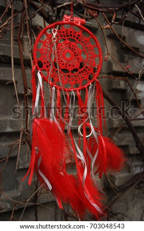 Red dream catcher with feathers on the background of a concrete wall and branches of grapes. Ethnic design, boho style, tribal symbol.