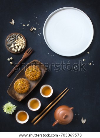 Flat lay conceptual mid autumn festival mooncake tea party table top shot on moody rustic blue background. Translation on round moon cake "Mid autumn". Royalty-Free Stock Photo #703069573
