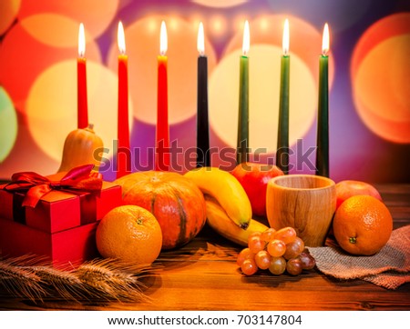 Kwanzaa festive concept with seven candles red, black and green, gift box, pumpkin, bowl and fruit on light blur bokeh background