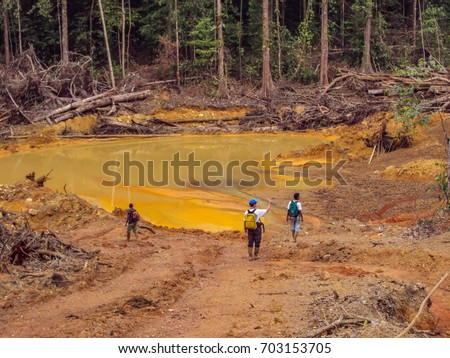 Gold mining place in Guyana. Waste water flows into the forest. Three men examine the effects of gold mining. Similar as in Brazil. Amazon and Essequibo basin deforestation. Rainforest destruction.  Royalty-Free Stock Photo #703153705