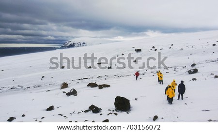 Snow covered landscape of Brown Bluff, Antarctic Peninsula. Cruise ship passengers walking among basalt boulders. Antarctica.