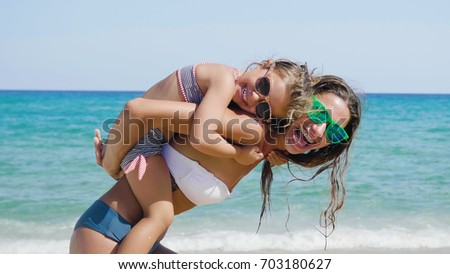 Mother and little daughter are having fun, playing on the sea, wearing sunglasses, hugging in swimsuits, background of sea blue water.