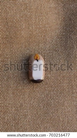ALANYA, TURKEY - 18 JANUARY 2014 - A LIGHT CANDLE PAINTED ON A PIECE OF TILE POLISHED BY THE SEA LYING ON  A CANVAS PATTERN