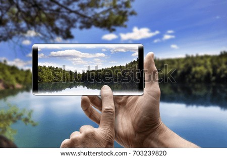 Two hands holding a mobile Smartphone and take a picture of Beautiful Serene Lakeview.