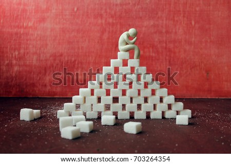   the concept of sugar  addiction / the figure of a man sitting  on the top of the pyramide of sugar cubes Royalty-Free Stock Photo #703264354