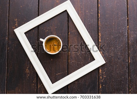 Cup of coffee in white frame on wooden floor