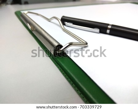 A green paper clip file with a black twist ball pen.