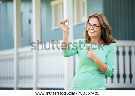 Happy woman holds the keys in her hand. In the background the house. 