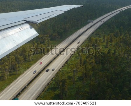Aerial shot of the long paved roads of Louisiana leading out of New Orleans, with an airplane wing in the picture
