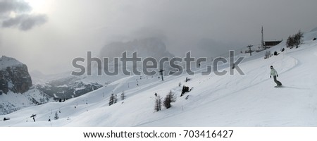 A girl riding snowboard in front of Langkofel Group mountains shrouded in dark clouds. Dolomite Alps (Sella Ronda). Italy.