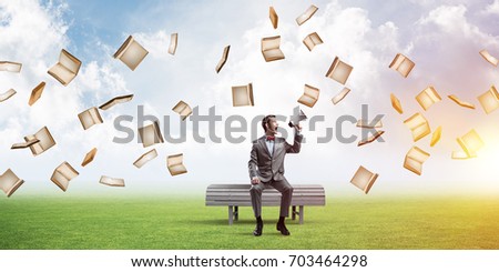 Young businessman sitting on bench and screaming emotionally in megaphone