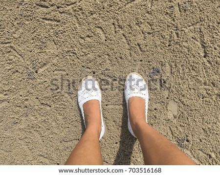 Woman wearing white shoes standing on the sand.