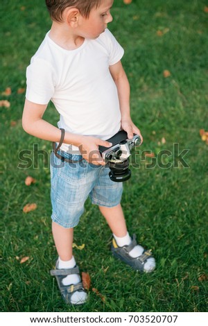 handsome little boy wearing shorts and sandals holding vintage film camera standing on green grass with fallen leaves