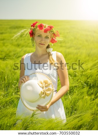 Beautiful woman with flowers poppies on the head in a field of green rye. Portrait of a beautiful woman on a background of green fields.