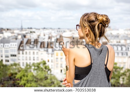 Young woman enjoying great view on Paris skyline standing on the terrace with coffee cup