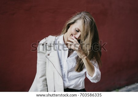 A young woman in white jacket posing near red wall. fashion shooting on the street