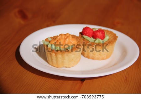 Two multi-colored small Cupcakes on a white plate on a wooden background. Concept:  dessert for breakfast