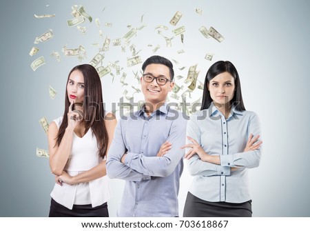 Smiling Asian man and his serious female colleagues are standing near a gray wall under a dollar rain.