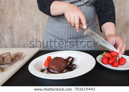 Cook woman decorates delicious chocolate dessert with strawberry. Process of making culinary art of fondant with fresh red berries