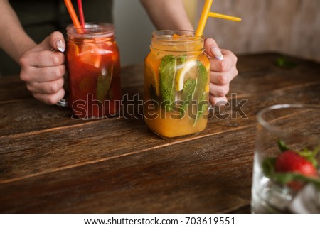 Waiter brings jars of fresh fruit cocktails to customer. Orange and strawberry cold drink with mint and ice on wooden table, refreshment and satisfying thirst in hot weather, free space