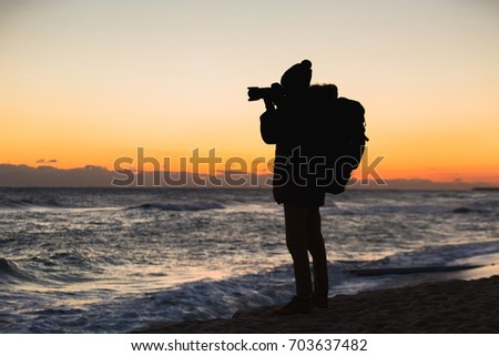 A traveler with a backpack is standing on the seashore and photographing the sunrise on Japan Sea, South Korea