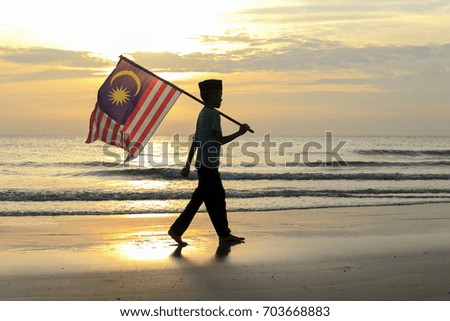 The Concept of Independence Day - a boy holding the Malaysian flag on the shore at sunrise