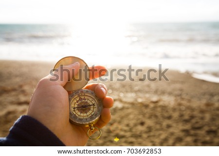 Point of view photo of man holding compass in the hand on the sea and beach background.