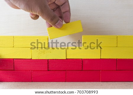 Two fingers put the last red block on the wall, Metaphoric scene,Building concept Royalty-Free Stock Photo #703708993