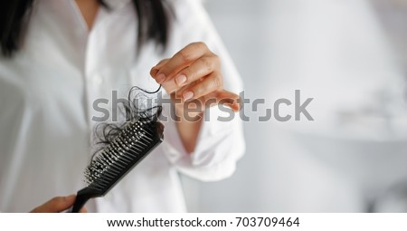 woman losing hair on hairbrush in hand, soft focus Royalty-Free Stock Photo #703709464