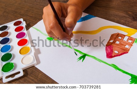 The child's hand draws a picture with watercolors