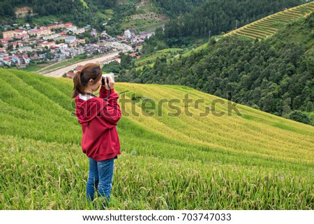 Female adventure backpack traveler taking a photograph of the nice view of rice terrace on the top of the mountain in Mu Cang Chai city near Sapa, Vietnam.