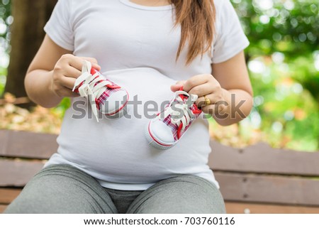 Young pregnant woman holding baby shoes to her belly