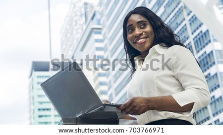 Portrait of happy business african woman uses computer laptop in the outdoor with the city space background