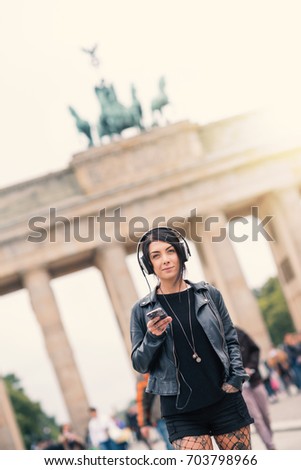 Young brunette woman with headphones in Berlin. Brandenburg Gate in the background. Flare backlight filtered image. Lifestyle concept. 