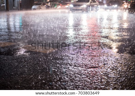 Puddle near the wet road in the rain.Heavy rain drops on asphalt.View from the level of asphalt level. Blured background of the night city traffic and traffic congestion concept.