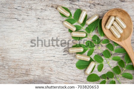 Herbal medicine in capsules from moringa leaf on rustic wooden table with copy space for medical background, healthy eating with natural product for good living  Royalty-Free Stock Photo #703820653
