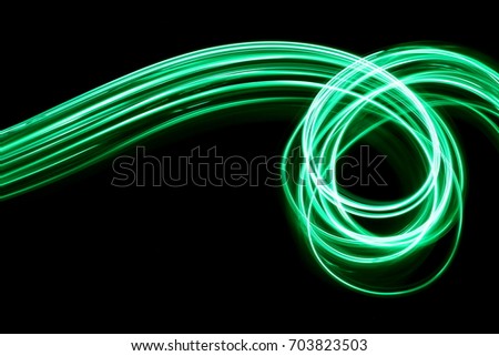 Green light painting, long exposure photography, loop and swirl pattern against a black background