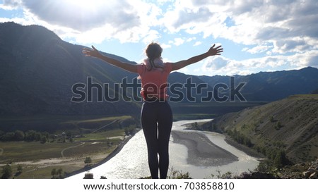 Woman standing on top of a mountain with hands rised up. Back view, travel and recreation. Royalty-Free Stock Photo #703858810