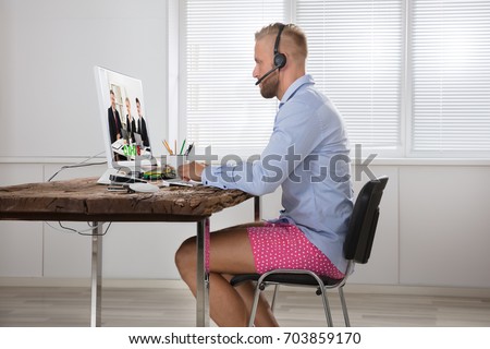 Businessman Dressed In Shirt And Shorts Having Video Call On Computer In The Home Office Royalty-Free Stock Photo #703859170